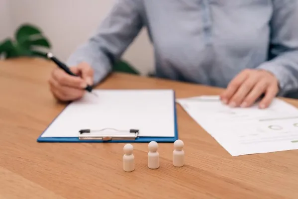 Hombre toma notas mientras observa una figura de madera, simbolizando decisiones clave ante el análisis en estudio socioeconómico laboral.