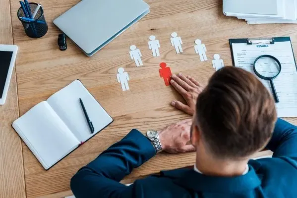 Un hombre sosteniendo un papel en forma de silueta de persona con color rojo, y siluetas personas hechas de papel de color blanco al rededor, haciendo la representación de servicios de reclutamiento monterrey